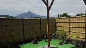 A spa area with a hot tub, bamboo fence, and a view of a mountain. - Fuji Sansuikan (Fujikawaguchiko)