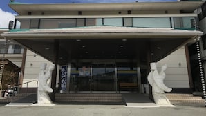 A building with a covered entrance, two white statues on either side, and a sign with Japanese characters. - Fuji Sansuikan (Fujikawaguchiko)