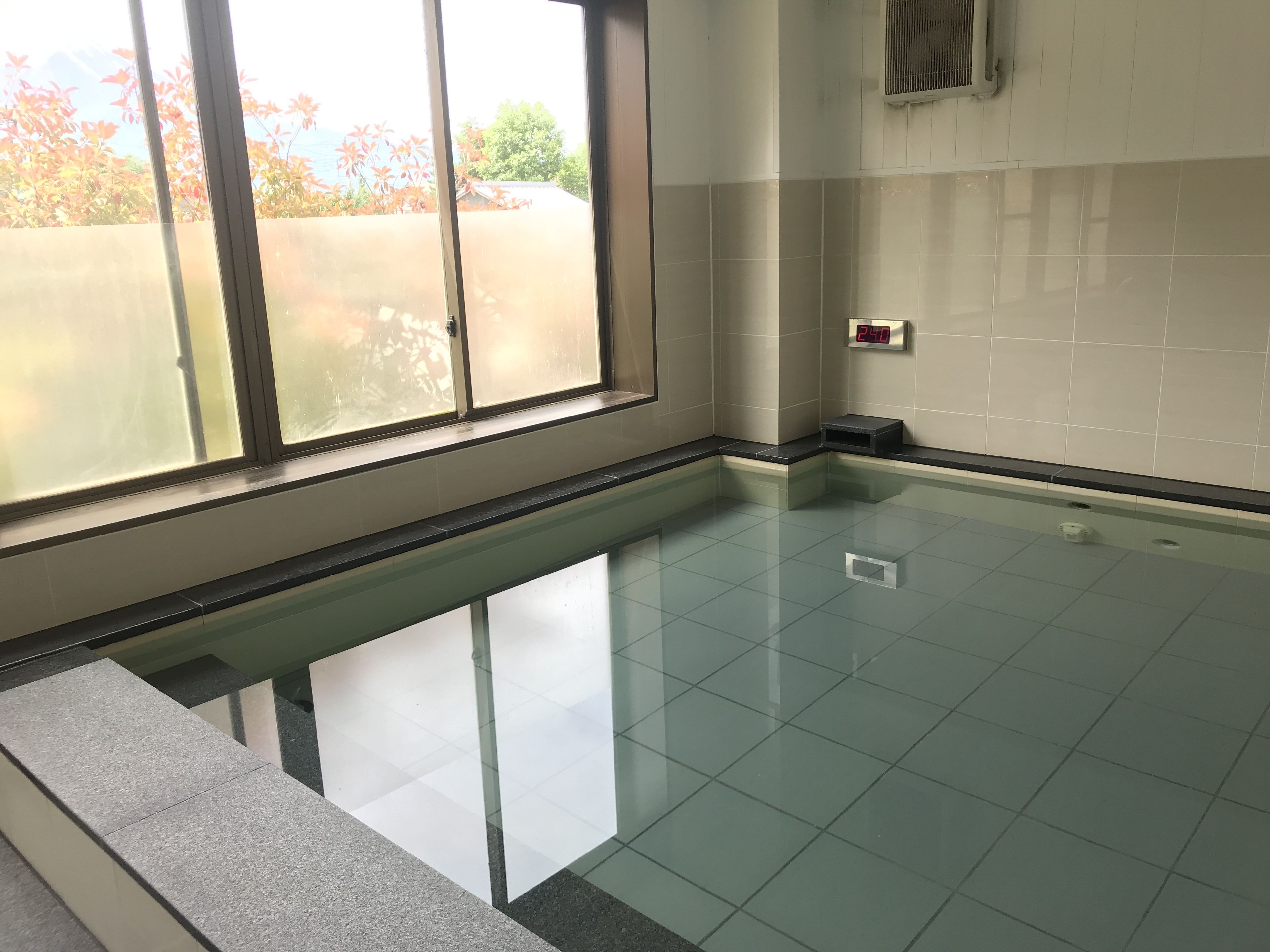 Ein Schwimmbecken mit klarem Wasser, einer gefliesten Wand und einem Fenster mit Sandstrahlglas.