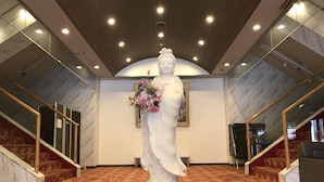 A statue of a robed figure holding a bouquet, surrounded by marble walls and a red carpeted floor. - Fuji Sansuikan (Fujikawaguchiko)