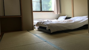 A room with tatami mats, a bed with white bedding, a window with a view of greenery, and a wooden wardrobe. - Fuji Sansuikan (Fujikawaguchiko)