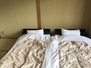 A double bed with a beige patterned duvet and white pillows, set against a plain wall with a wooden beam. - Fuji Sansuikan (Fujikawaguchiko)
