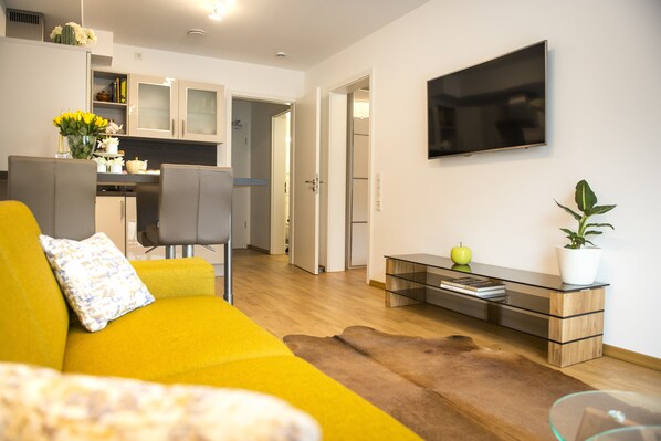 A modern living room with a yellow sofa, a glass coffee table, and a mounted TV.