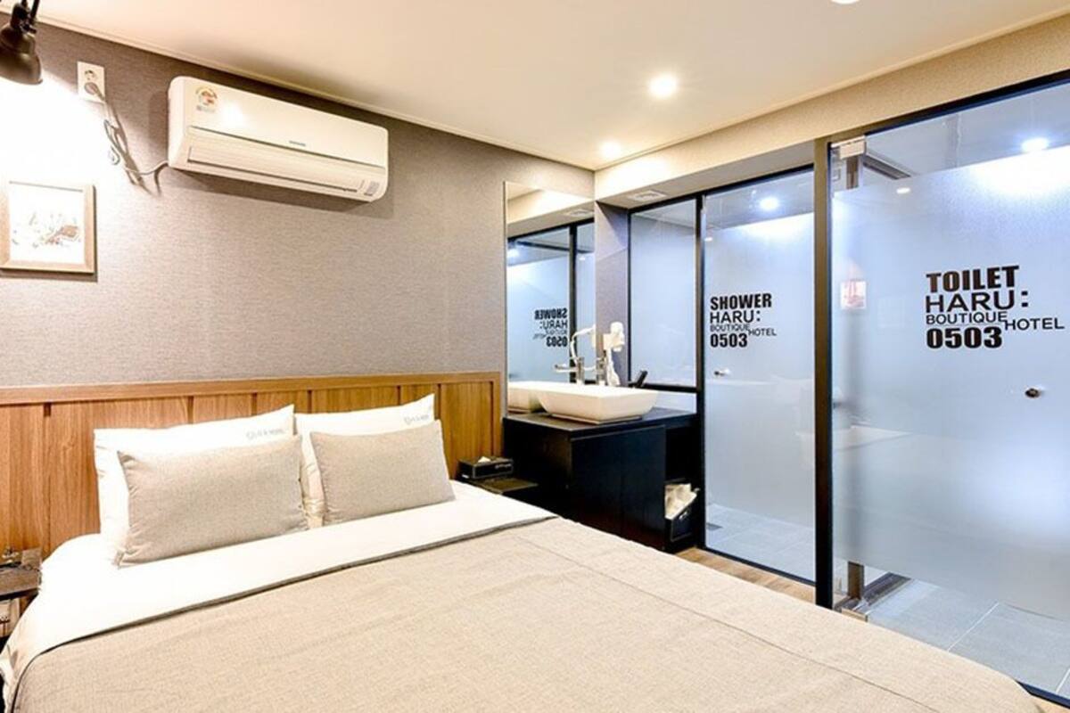 A hotel room with a bed, bedside table, and a glass partition with a shower area.