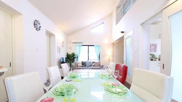 Un comedor con una mesa de vidrio preparada para seis personas, sillas blancas y una silla roja.