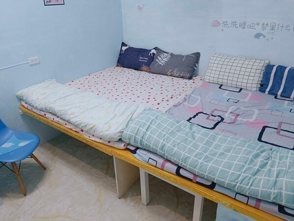 Una cama individual con una colcha estampada, una silla azul y una pared de color azul claro con algo de texto.