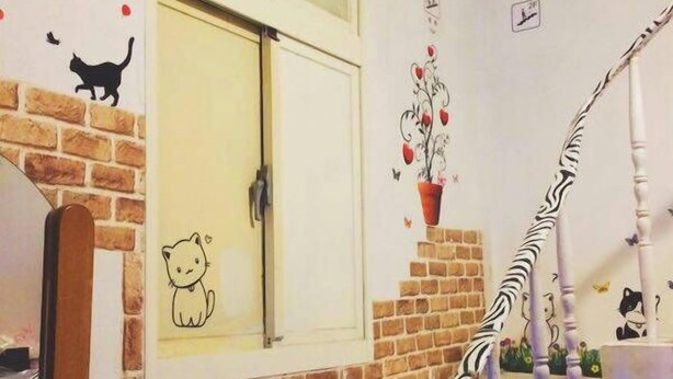 A staircase with a zebra-striped handrail, a brick wall, and a window with a cat decal. - XIAN BnB (Jinhu)