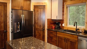 Une cuisine moderne avec des meubles en bois, un réfrigérateur en acier inoxydable, un plan de travail en granit et une fenêtre donnant sur la forêt.