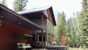 Une cabane à deux étages dotée d’un porche couvert, de meubles d’extérieur et offrant une vue sur une zone boisée.