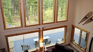 Une cabane dotée de grandes fenêtres donnant sur la forêt, d’un ventilateur de plafond et d’une terrasse avec des sièges d’extérieur.
