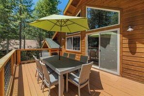A wooden deck with a table and chairs, a green umbrella, and a large window.