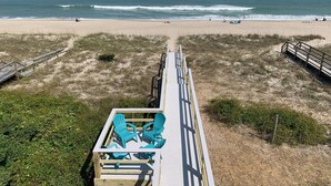 Een uitzicht op het strand met een houten looppad dat leidt naar een zitgedeelte met blauwe stoelen.