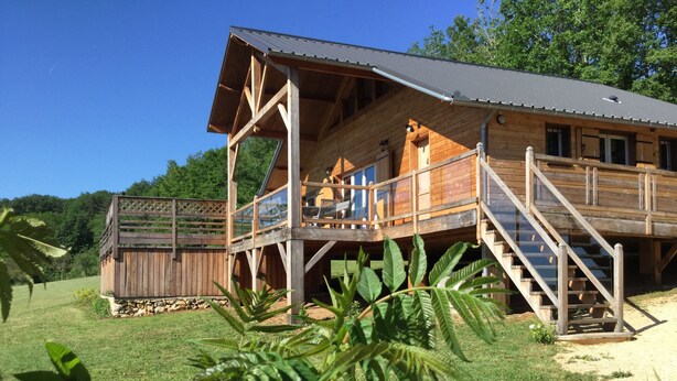 A wooden cabin with a balcony, a staircase, and a fenced area.