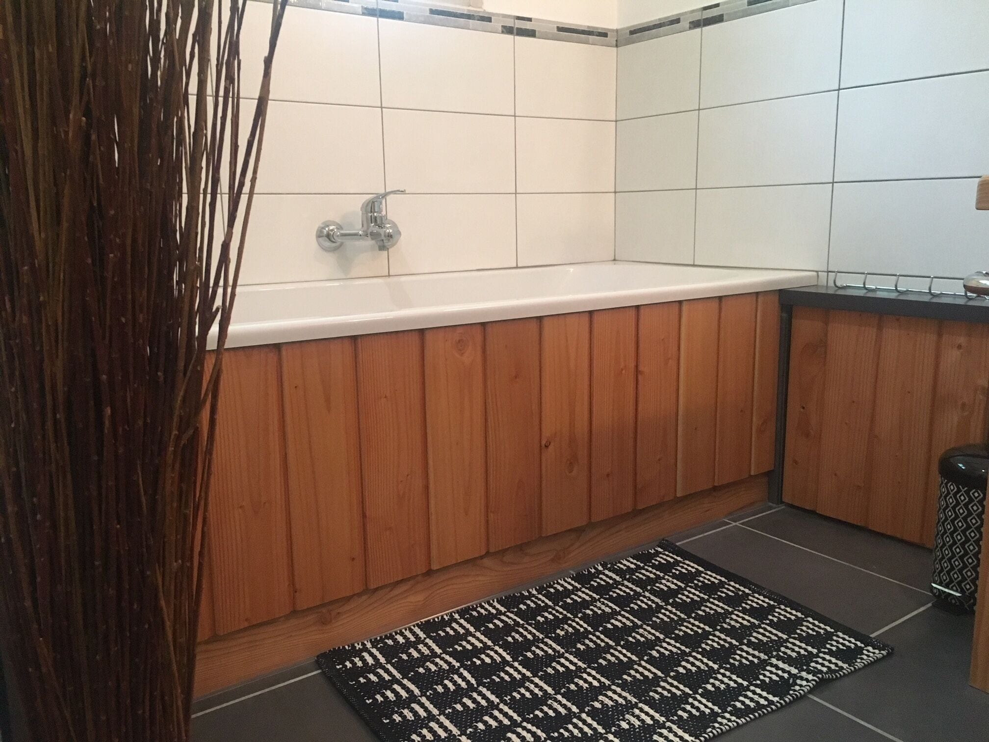 Une salle de bain avec un meuble-lavabo en bois, une baignoire blanche et un tapis à motifs noir et blanc.