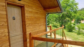 A wooden cabin with a glass balcony, a wooden door, and a wooden staircase leading to the balcony.
