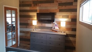 Una habitación con pared de madera, televisor de pantalla plana, dos lámparas de pared y un aparador, además de una pequeña maqueta de un velero.