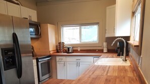 Una cocina con encimera de madera, electrodomésticos de acero inoxidable, armarios blancos y un ventanal que proporciona luz natural.