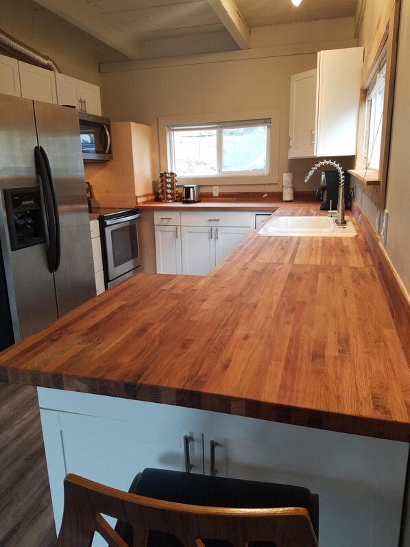 A kitchen with a wooden countertop, stainless steel appliances, white cabinets, and a window providing natural light.