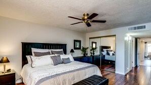 Une chambre avec un grand lit, un ventilateur de plafond, un plancher en bois et un banc.
