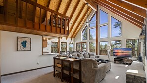 A spacious living room with a high ceiling and large windows, a cozy sofa, a wooden coffee table, and a flat-screen TV. - Basque Haus at Northstar:Beautiful A-Frame Minutes to Golf, Mtn Biking and Tahoe (Truckee)