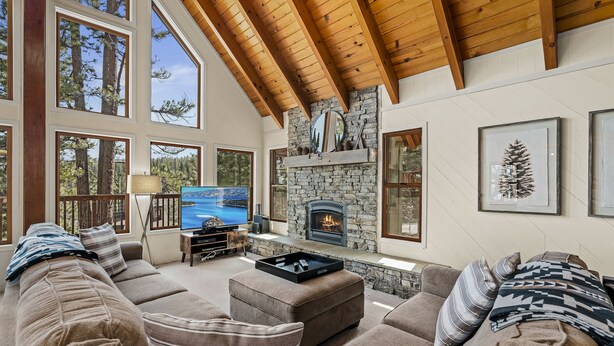 A cozy living room with a stone fireplace, large windows, and a wooden ceiling. - Basque Haus at Northstar:Beautiful A-Frame Minutes to Golf, Mtn Biking and Tahoe (Truckee)