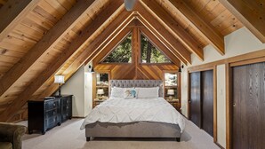 A bedroom with a vaulted ceiling, a bed with a white quilt, a dresser, and a nightstand with a lamp. - Basque Haus at Northstar:Beautiful A-Frame Minutes to Golf, Mtn Biking and Tahoe (Truckee)