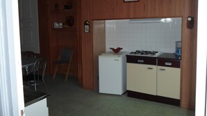 Een kleine keuken met houten lambrisering, een koelkast, een fornuis en een spoelbak.