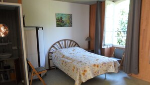 Een slaapkamer met een bed, een stoel, een bureau, een raam en een schilderij aan de muur.