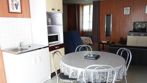 Een kleine keuken met een magnetron, een spoelbak en een kastje. Er is een zithoek met een ronde tafel en vier stoelen.