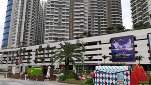 A modern hotel with multiple high-rise buildings in the background, a central courtyard with palm trees, and a colorful ice cream-themed kiosk.