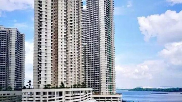 A high-rise residential building with multiple balconies, a swimming pool area with a fountain, and a beach view.