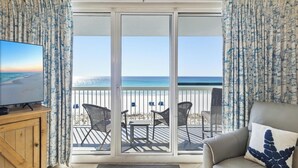 Una stanza con una televisione su un mobile in legno, un divano con un cuscino a forma di stella, e un balcone con sedie in vimini e un tavolino.