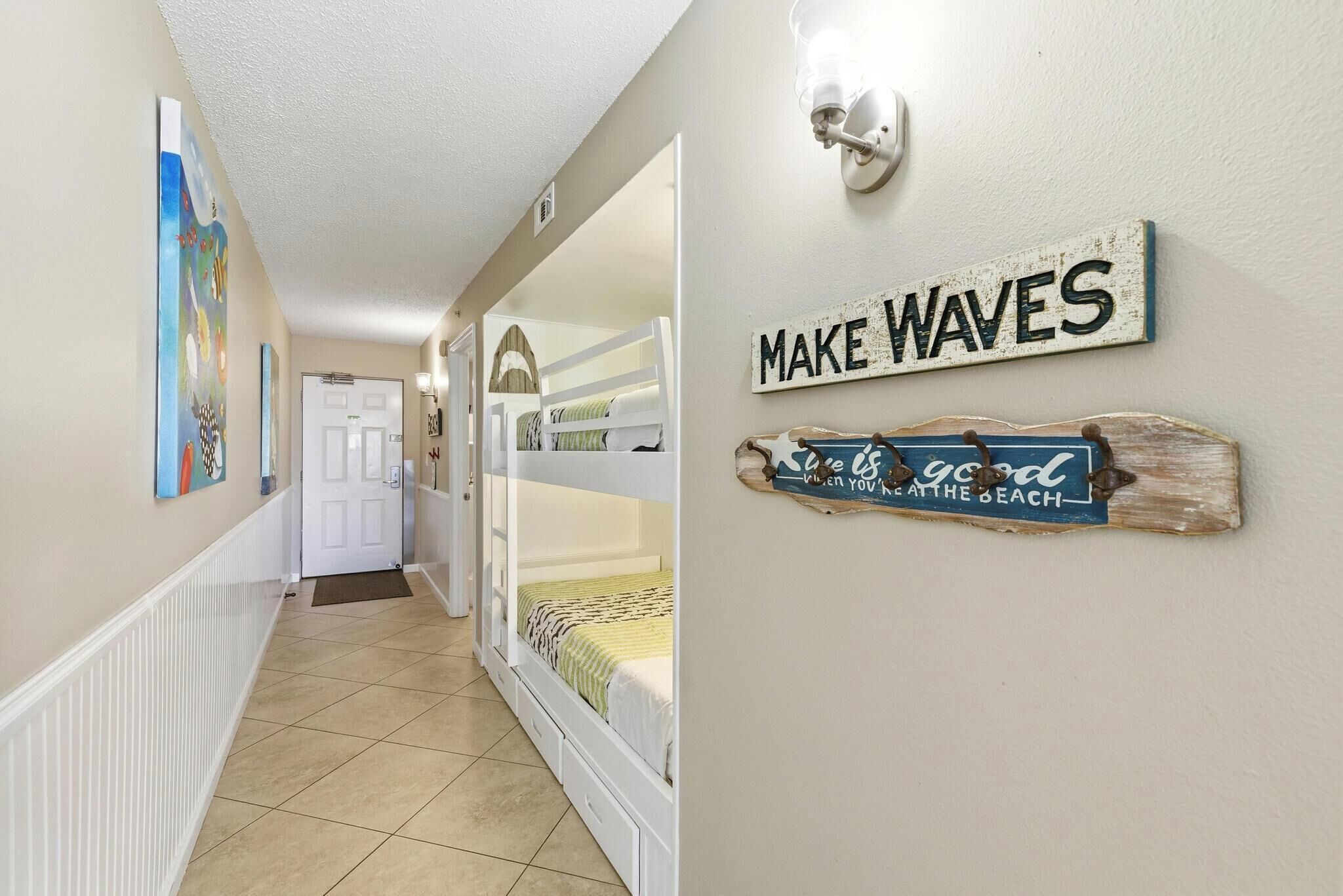 A hallway with bunk beds, a door, and wall decorations including a sign that says "MAKE WAVES".