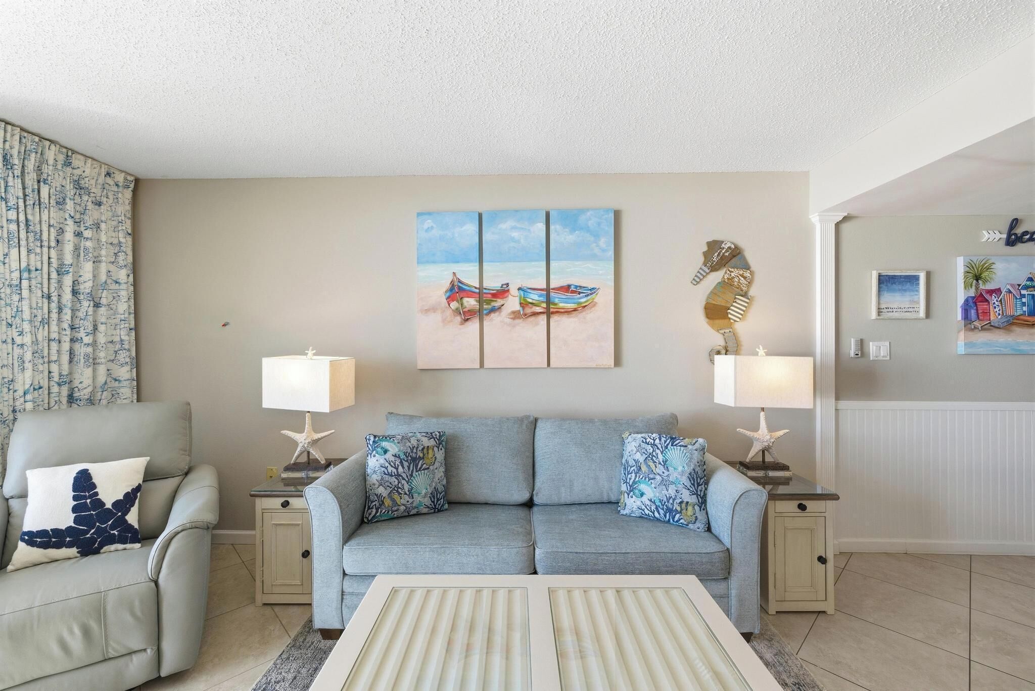 Ein Wohnzimmer mit einem grauen Sofa, zwei passenden Beistelltischen, einem Streifen-Teppich und einem Strandbild über dem Sofa.
