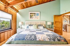 A bedroom with a wooden ceiling, a large bed with a quilt, two bedside lamps, and a framed picture on the wall.