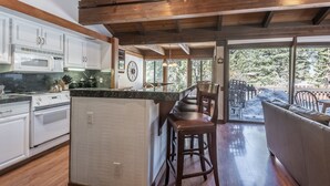 Une cuisine avec des meubles blancs, un îlot central doté de tabourets et une vue sur un espace de détente extérieur.