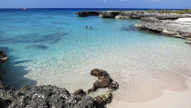 Een strand met helder turquoise water, rotsformaties en een boot in de verte.