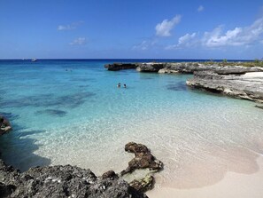 Een strand met helder turquoise water, rotsformaties en een boot in de verte.