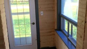 A wooden interior with a door leading to a balcony, a window, and a light switch on the wall. - GRINDSTONE PARK, minutes from water & Beach. Hunting and fishing Largest MOOSE (Riverton)