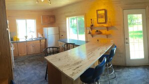 A kitchen with wooden cabinets, a refrigerator, a sink, a dining table with chairs, and a window providing natural light. - GRINDSTONE PARK, minutes from water & Beach. Hunting and fishing Largest MOOSE (Riverton)