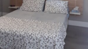 Un dormitorio con cama, ventilador de techo, un cuadro en la pared y mesita de noche.