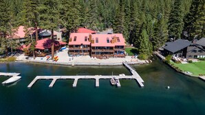 A lodge with a red roof, a dock, and a lake surrounded by dense forest. - Donner Vista: Lakefront Condo with Boat Slip, Sandy Beach and Unbeatable Views (Truckee)