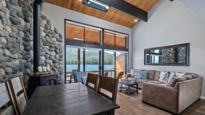 A spacious living room with a stone wall, large windows, a wooden ceiling, and a cozy seating area. - Donner Vista: Lakefront Condo with Boat Slip, Sandy Beach and Unbeatable Views (Truckee)