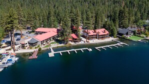 An aerial view of a lakeside lodge with multiple buildings, a dock, and a forested mountain backdrop. - Donner Vista: Lakefront Condo with Boat Slip, Sandy Beach and Unbeatable Views (Truckee)
