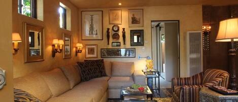 A living room with a beige sofa, a striped armchair, and a coffee table with books and fruit.