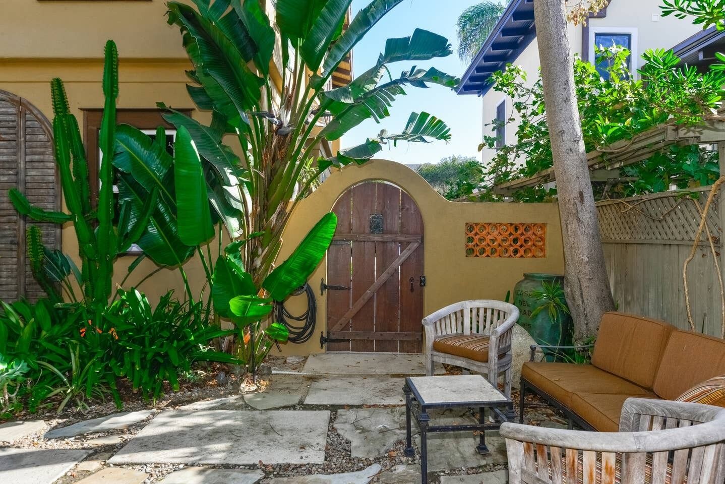 Une terrasse avec un sol en pierre, une porte en bois et une chaise blanche avec un coussin.