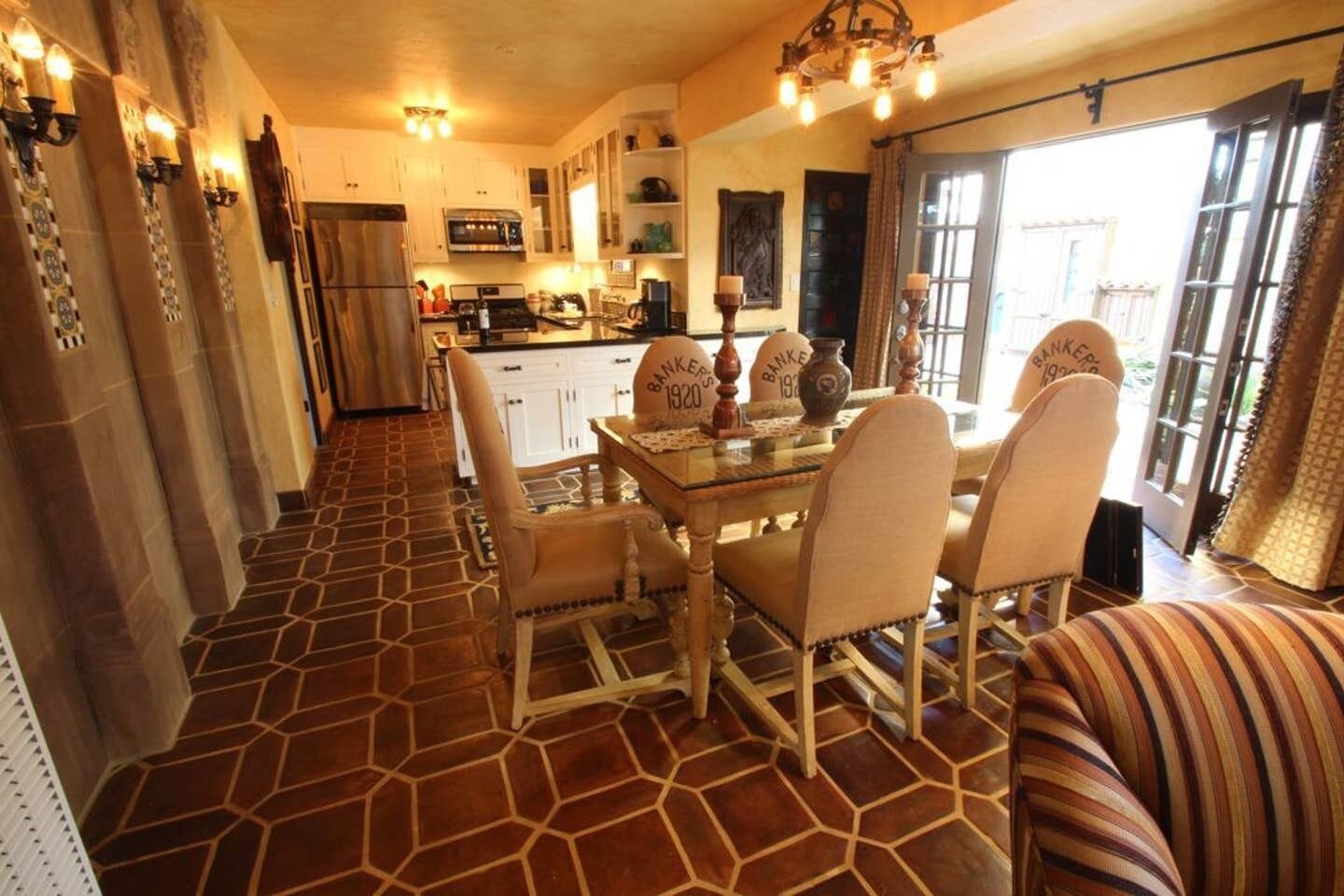 A dining area with a hexagonal tiled floor, a central table with chairs, and a chandelier.