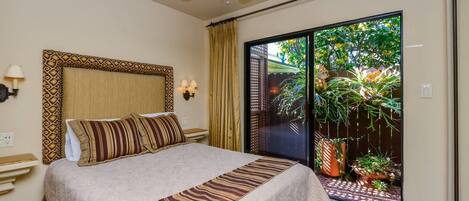 A bedroom with a bed, a ceiling fan, a nightstand, a wall-mounted lamp, and a view of a garden through a sliding door.