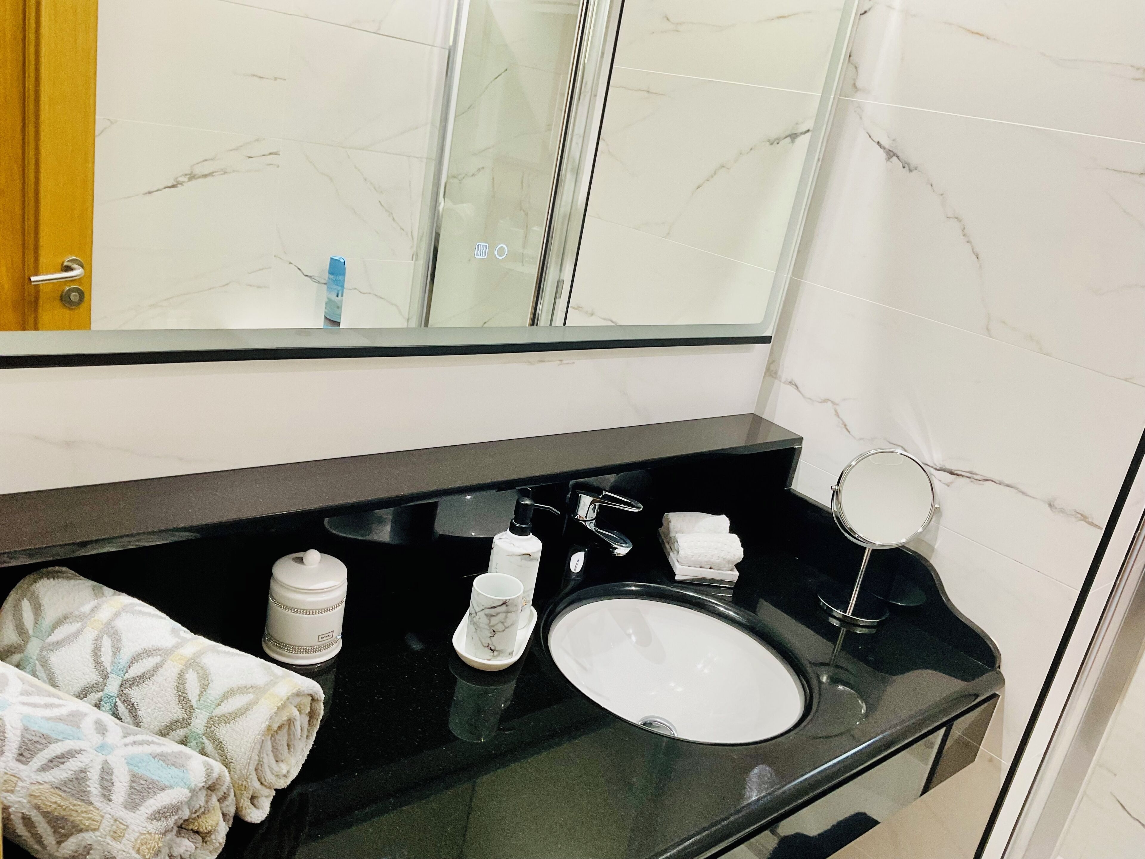 A bathroom with a black countertop, white marble tiles, a mirror, a sink, and towels.