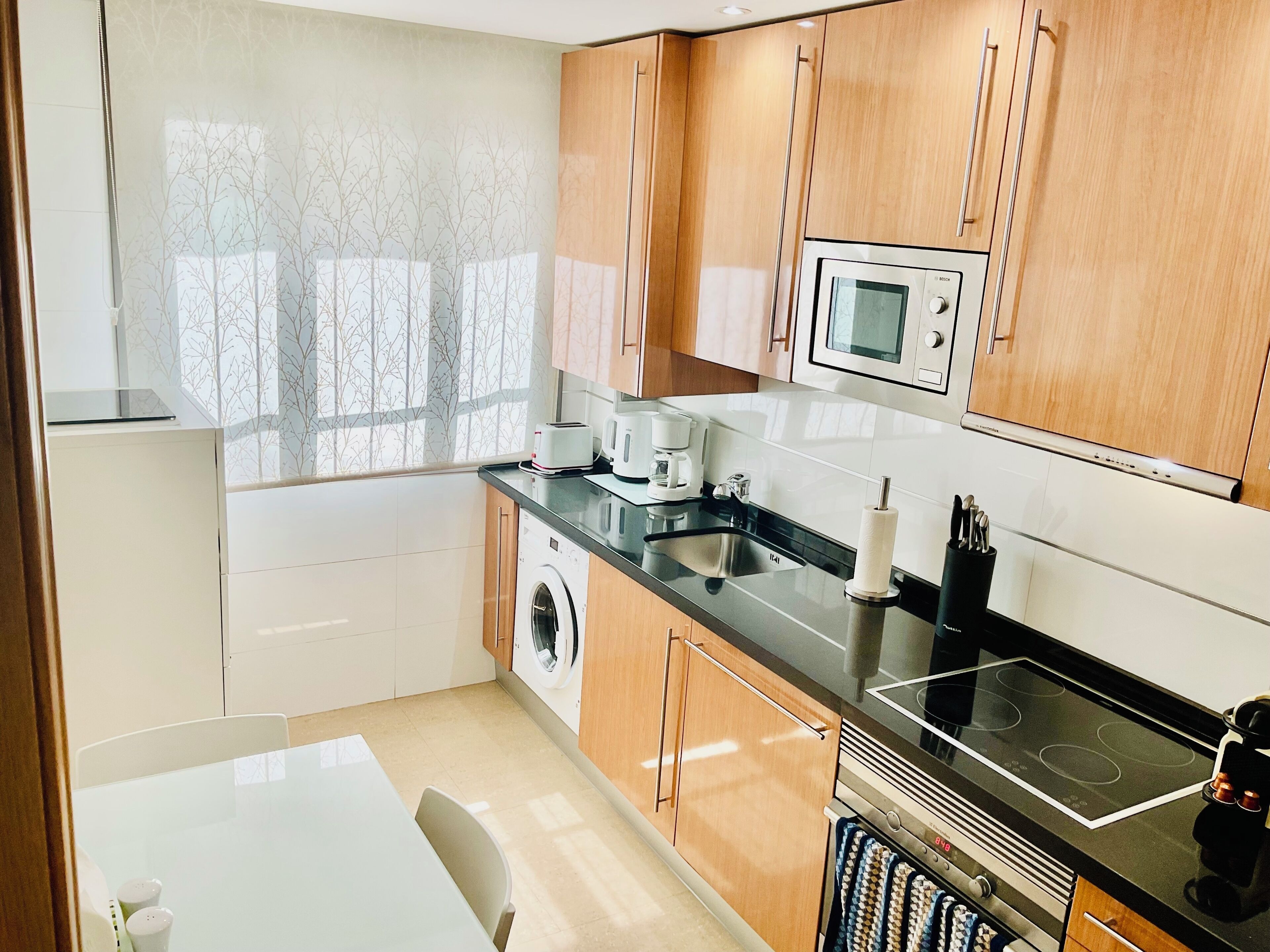 A modern kitchen with wooden cabinets, a built-in microwave, a stove, and a washing machine.
